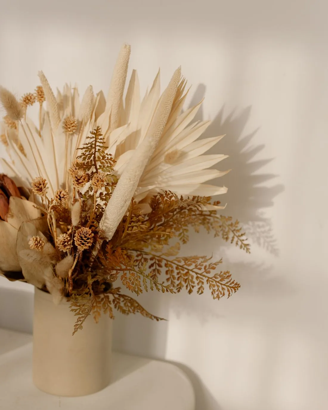Dried palm fronds in a pale ceramic vase against a warm cream wall
